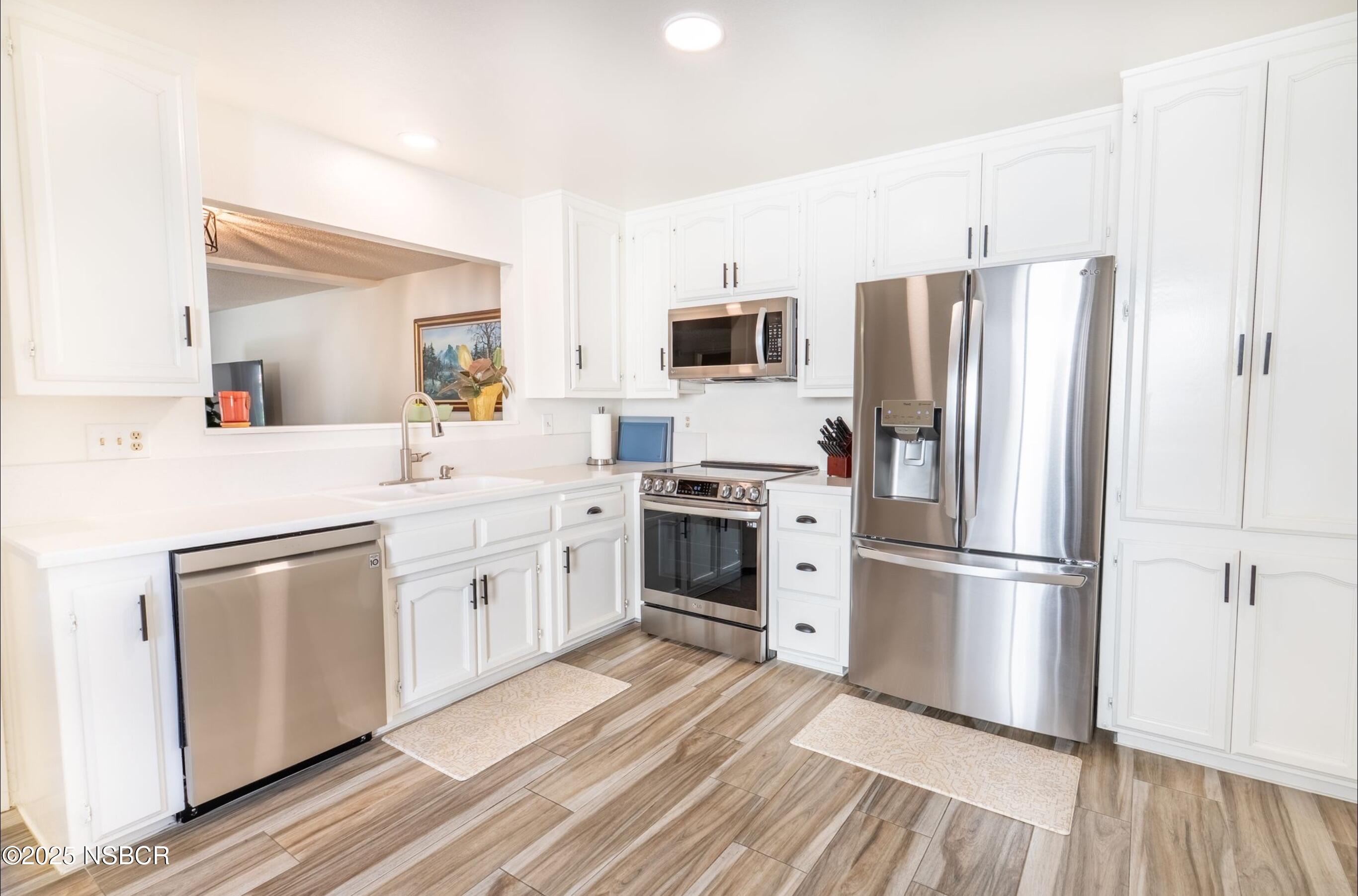 5 Stanford Circle Lompoc, CA 93436 - Photo 4 of 21 a kitchen with a refrigerator a stove a sink and white cabinets with wooden floor