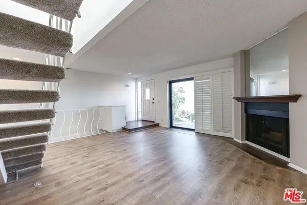a view of an empty room with wooden floor fireplace and a window