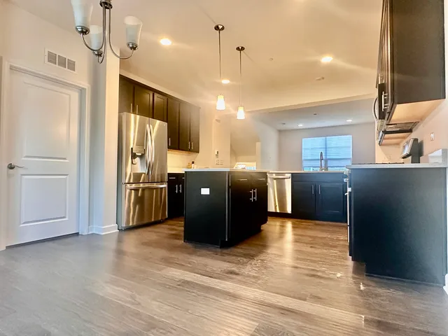 a kitchen with stainless steel appliances kitchen island granite countertop a refrigerator a sink dishwasher and a refrigerator with wooden floor