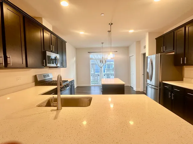 a large kitchen with stainless steel appliances a large counter top a stove a refrigerator a sink with a fireplace and wooden floors