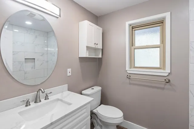 a bathroom with a toilet a sink a mirror and a window