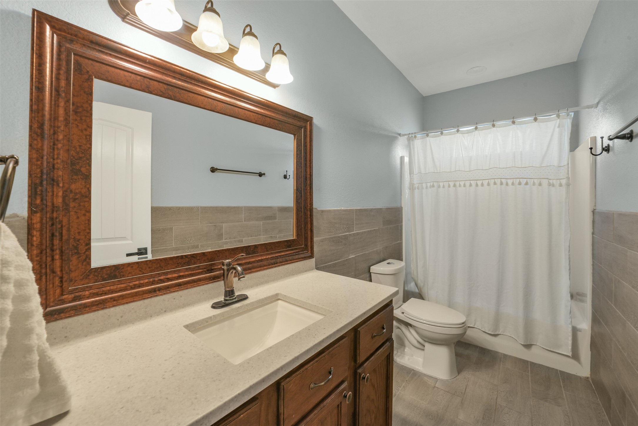 11301 South FM 441 Road El Campo, TX 77437 - Photo 17 of 43 This bathroom features a modern design with a large wooden-framed mirror, sleek countertop, and ample cabinet storage. It includes a tub/shower combo with neutral tile accents.