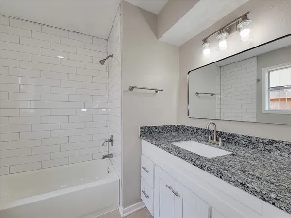 a bathroom with a granite countertop sink a mirror a bathtub and shower
