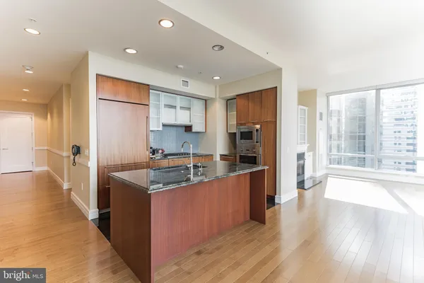 a kitchen with stainless steel appliances granite countertop a refrigerator a sink dishwasher a stove and a dining table with wooden floor