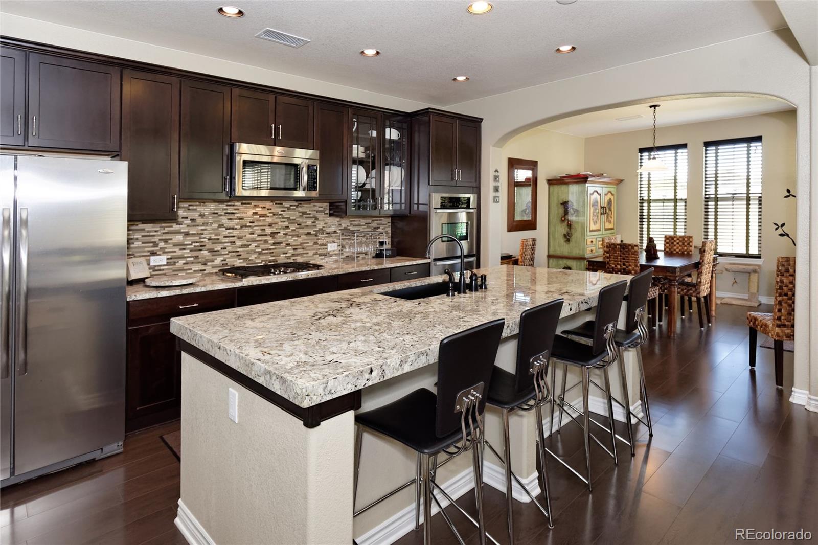 9278 Viaggio Way Highlands Ranch, CO 80126 - Photo 8 of 35 a kitchen with stainless steel appliances granite countertop a table chairs sink refrigerator and microwave