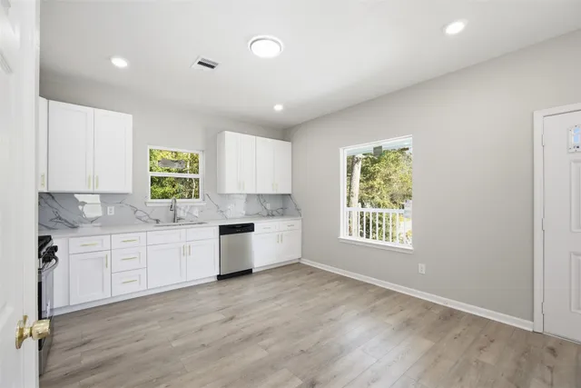 a large kitchen with granite countertop a stove a sink a window and white cabinets