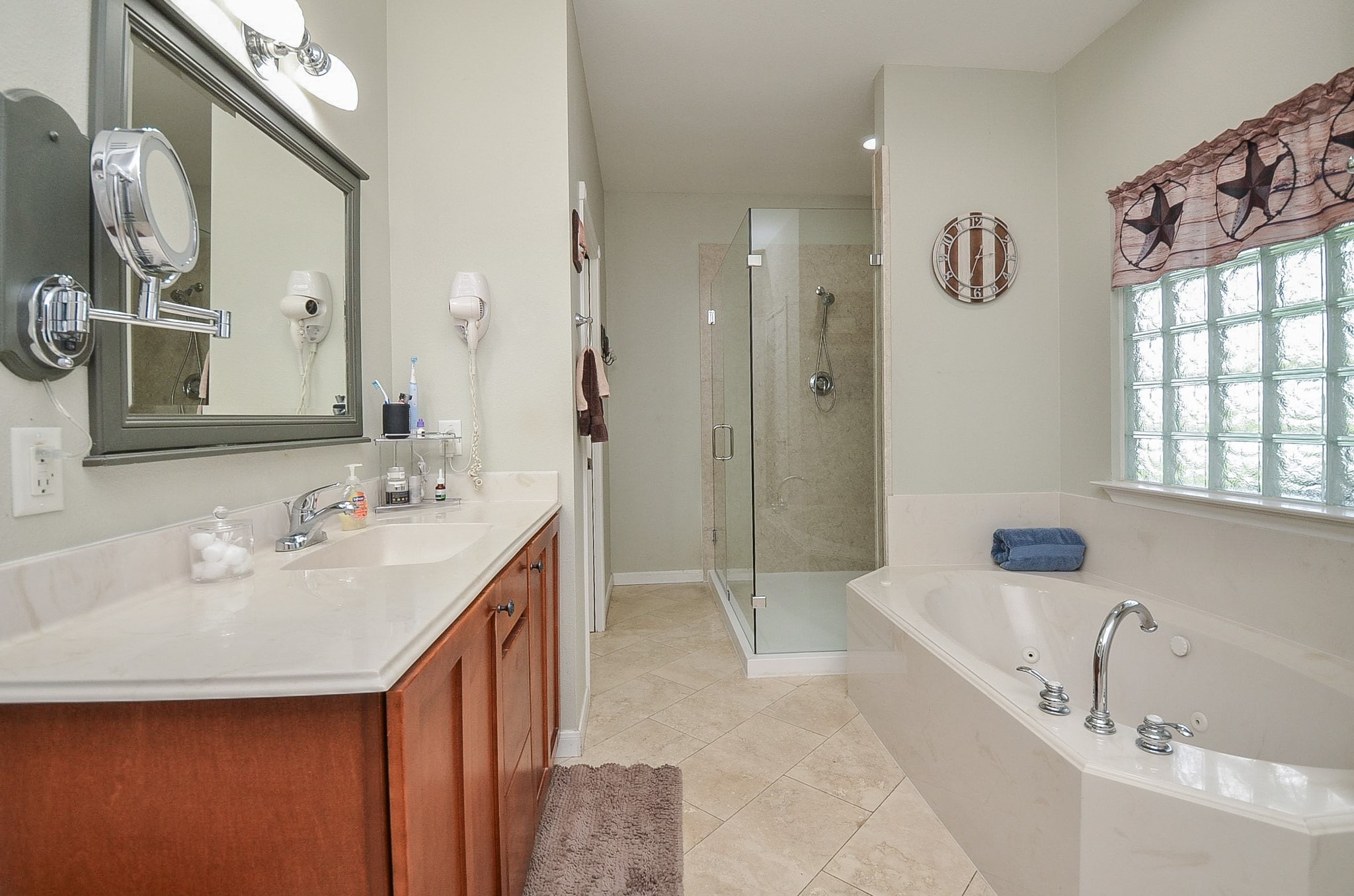 27644 Spring Hill Road Hempstead, TX 77445 - Photo 24 of 50 Clean, streamlined and comfortable paths line your primary ensuite bath; with lush honey colored cabinetry (left); pale earth toned walls, quaint art deco-like window above the generous soaking tub; with clear glass enclosed shower, up right.