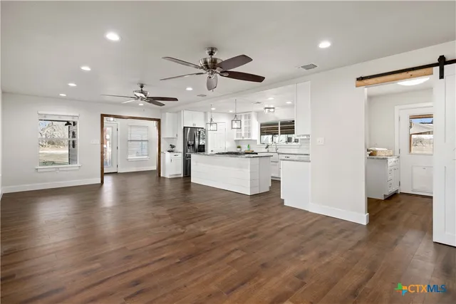 a view of an empty room and kitchen with wooden floor and a window