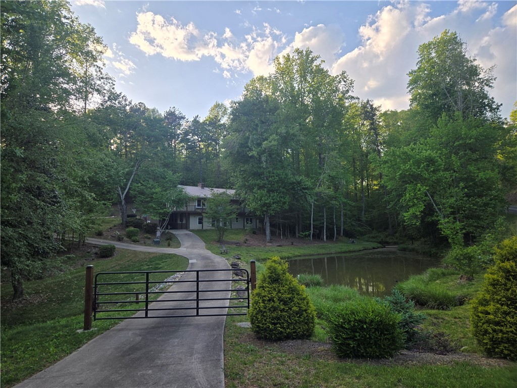 Nestled in a verdant landscape, a private drive leads to a charming residence beside a tranquil pond.