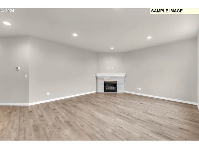 a view of an empty room with wooden floor and fireplace