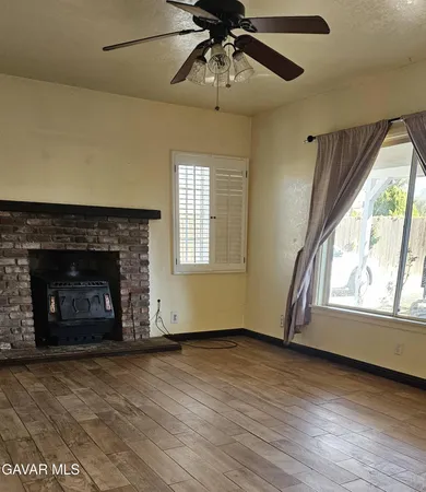an empty room with windows a fireplace a ceiling fan and wooden floor