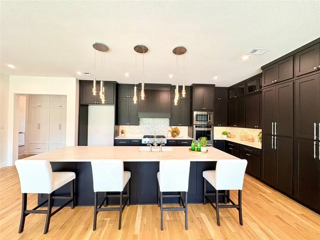 a kitchen with stainless steel appliances kitchen island granite countertop a dining table chairs and a refrigerator