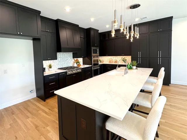 a kitchen with stainless steel appliances kitchen island granite countertop a refrigerator a stove and a sink with wooden floor