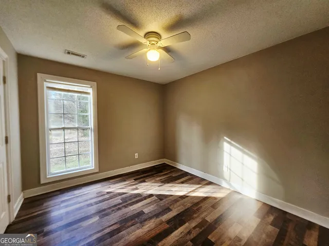 an empty room with wooden floor fan and windows