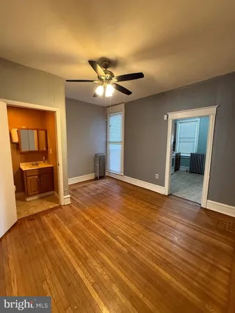 a view of an empty room with wooden floor and a ceiling fan