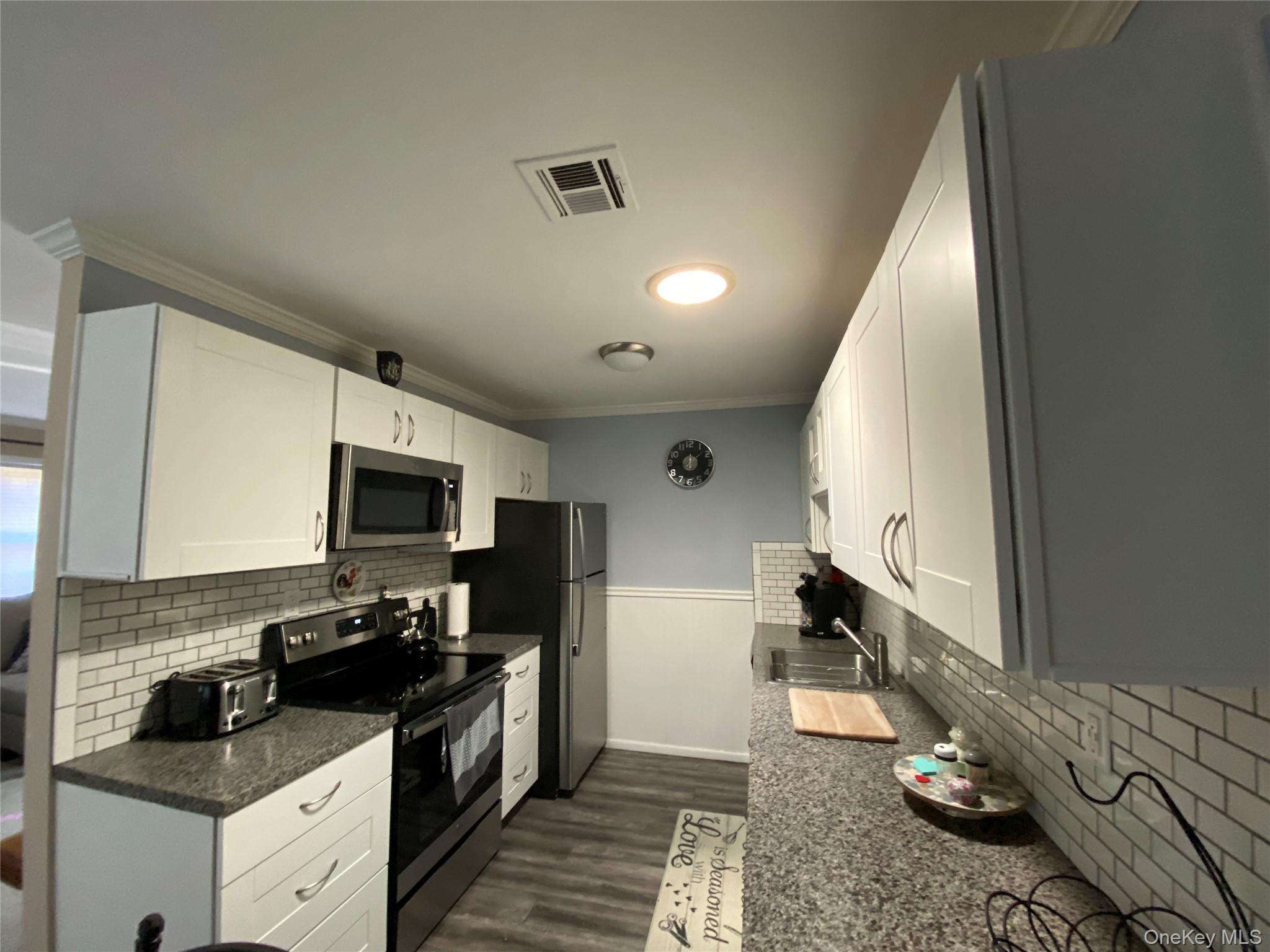 274 Berwick Court, Unit A Ridge, NY 11961 - Photo 14 of 31 Kitchen featuring backsplash, appliances with stainless steel finishes, white cabinets, dark wood-style floors, and ornamental molding