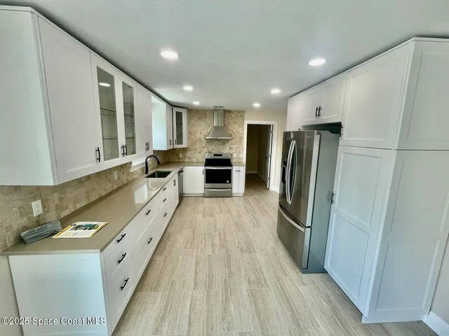 a large kitchen with stainless steel appliances granite countertop a refrigerator a sink dishwasher a stove and white countertops with wooden floor