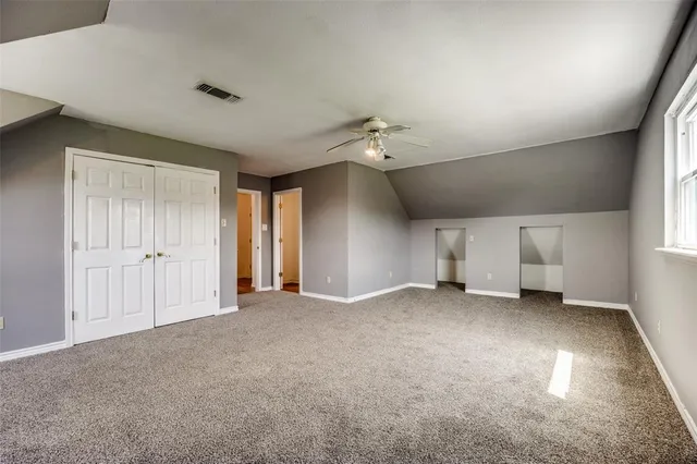 an empty room with chandelier fan and windows