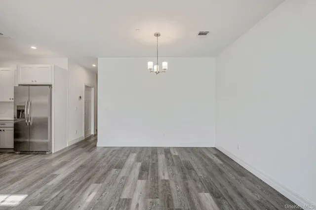 a view of empty room with wooden floor and kitchen view