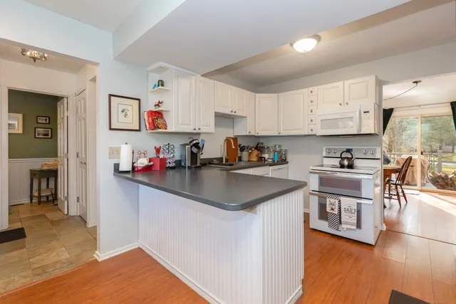 a kitchen with stainless steel appliances granite countertop a refrigerator a sink dishwasher a stove and white countertops with wooden floor