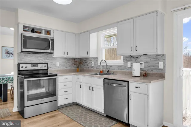 a kitchen with stainless steel appliances granite countertop white cabinets a sink a stove and a microwave