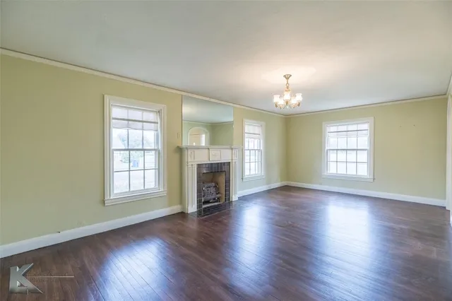 an empty room with wooden floor fireplace and windows