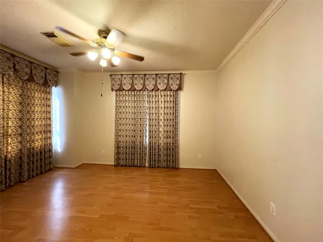 an empty room with wooden floor fan and windows