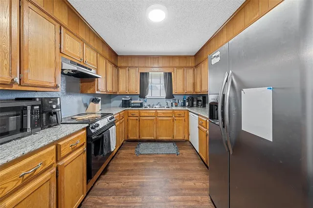 a kitchen with stainless steel appliances granite countertop a stove top oven a sink and dishwasher a refrigerator with wooden floor