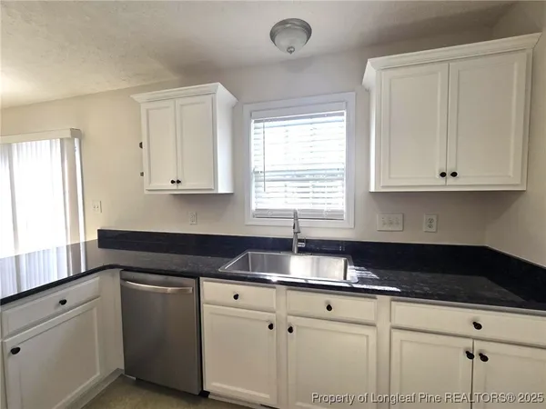 a kitchen with granite countertop white cabinets sink and window