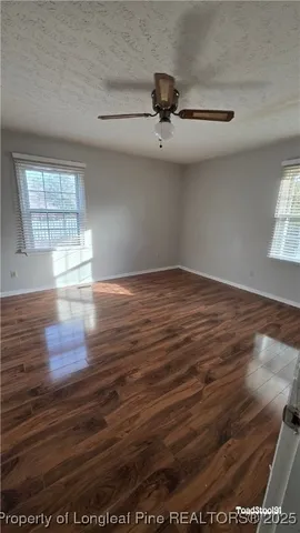 an empty room with wooden floor fan and windows