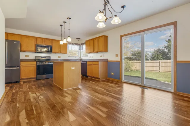 a open kitchen with granite countertop a stove top oven a sink dishwasher a dining table and chairs with wooden floor