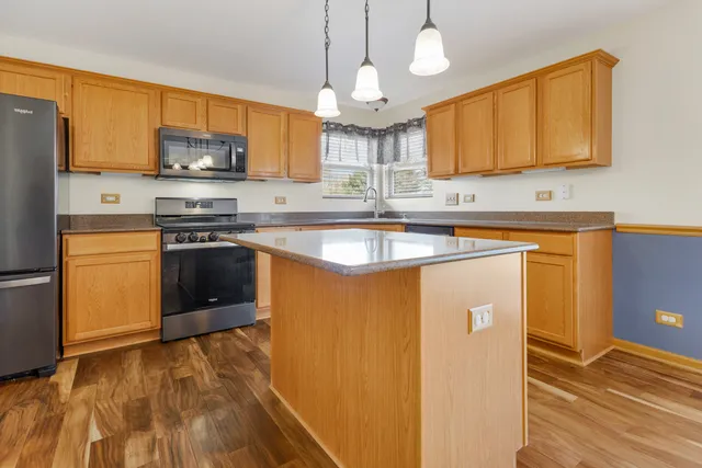 a kitchen with stainless steel appliances granite countertop a sink a stove a refrigerator cabinets and a dining table
