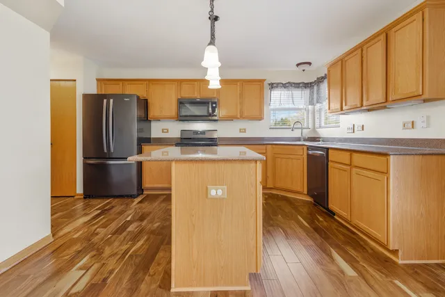 a kitchen with wooden cabinets a sink a stove a refrigerator and island with wooden floor