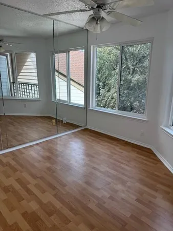 an empty room with wooden floor fan and windows