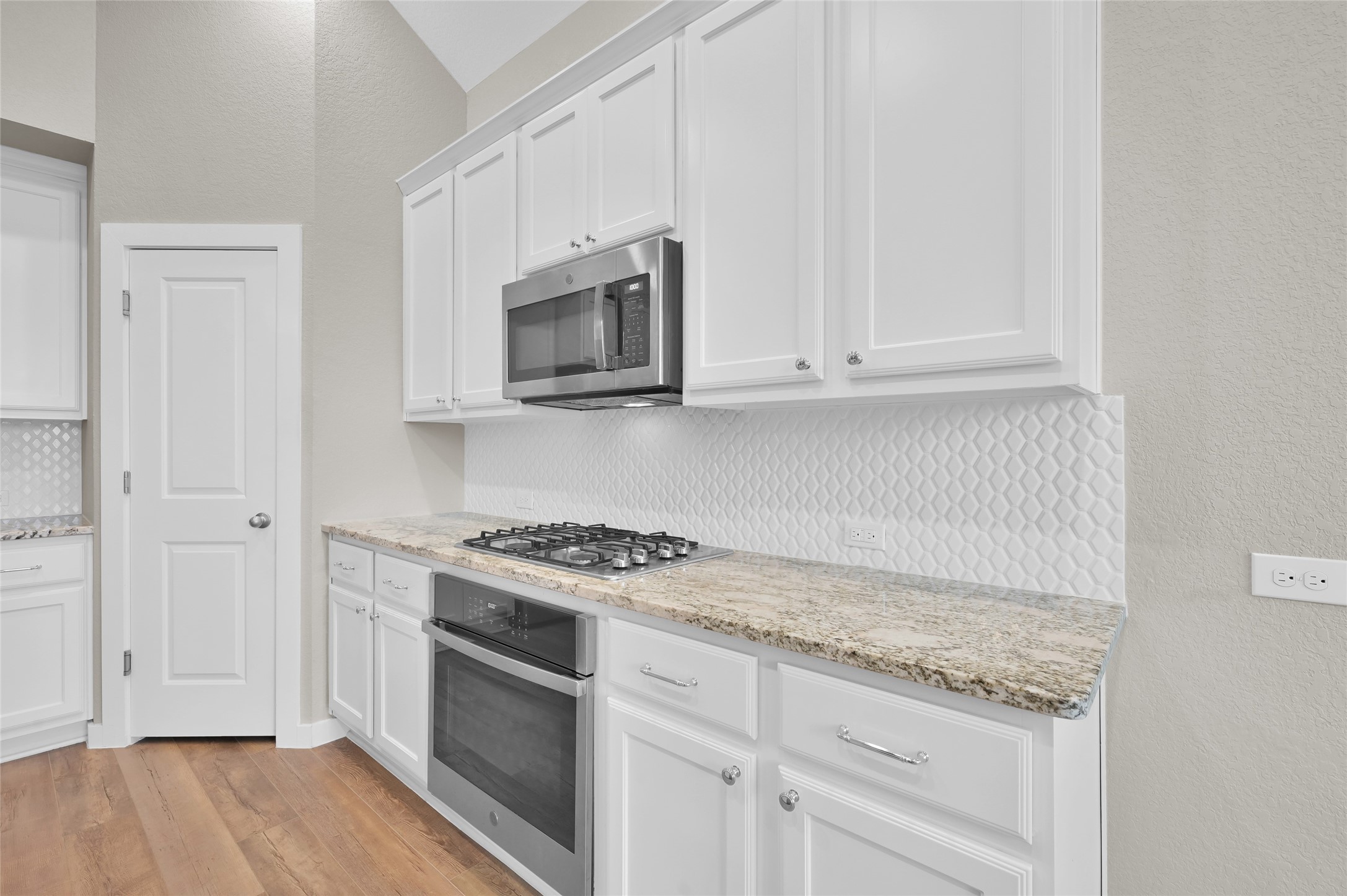 14960 Scarlet Branch Drive Conroe, TX 77302 - Photo 16 of 50 Close-up of the kitchen's gas cooktop, built-in microwave, granite counters, and full-height textured tile backsplash—clean and modern with plenty of cabinet storage.