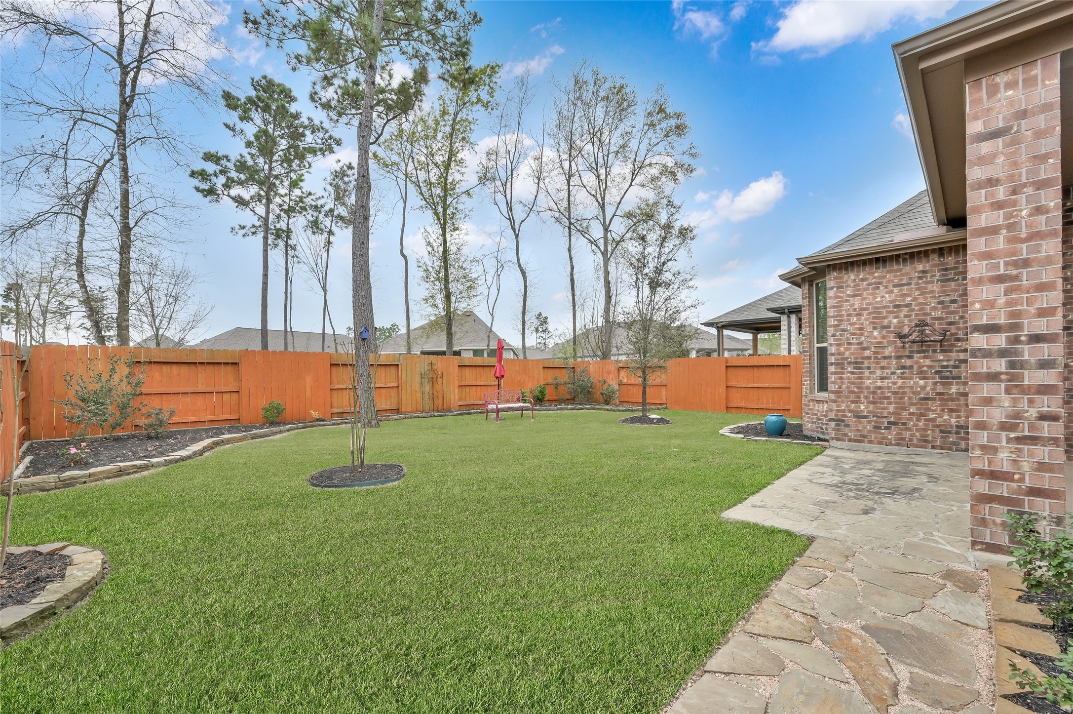 14960 Scarlet Branch Drive Conroe, TX 77302 - Photo 37 of 50 Spacious backyard with lush green lawn, stone walkway, and mature trees. Fully fenced with fresh landscaping—ideal for relaxing or entertaining outdoors.