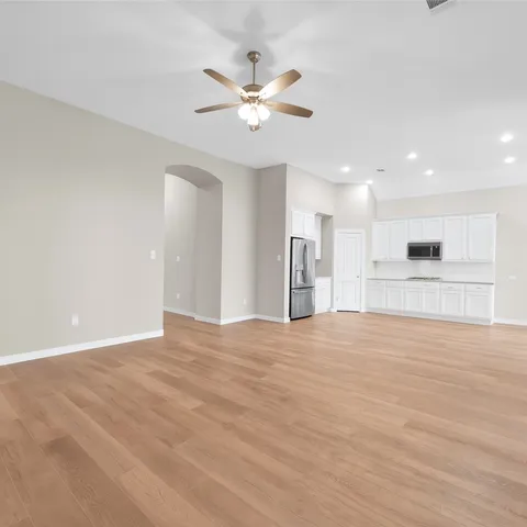 a large white kitchen with stainless steel appliances granite countertop a stove a sink a refrigerator and white cabinets with wooden floor