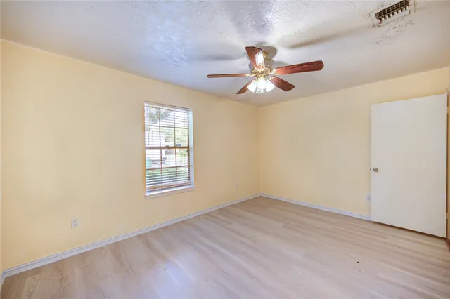 an empty room with wooden floor fan and windows
