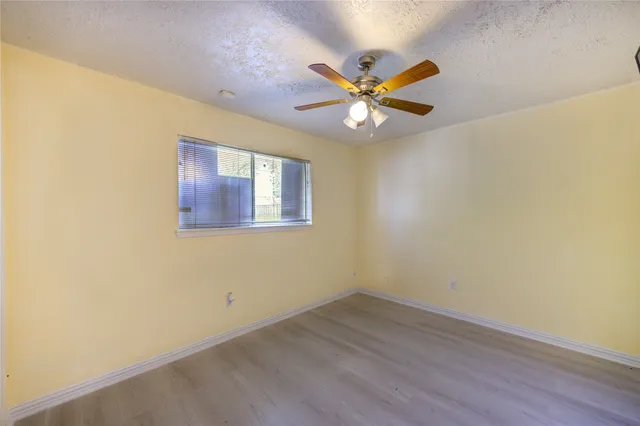an empty room with wooden floor fan and windows