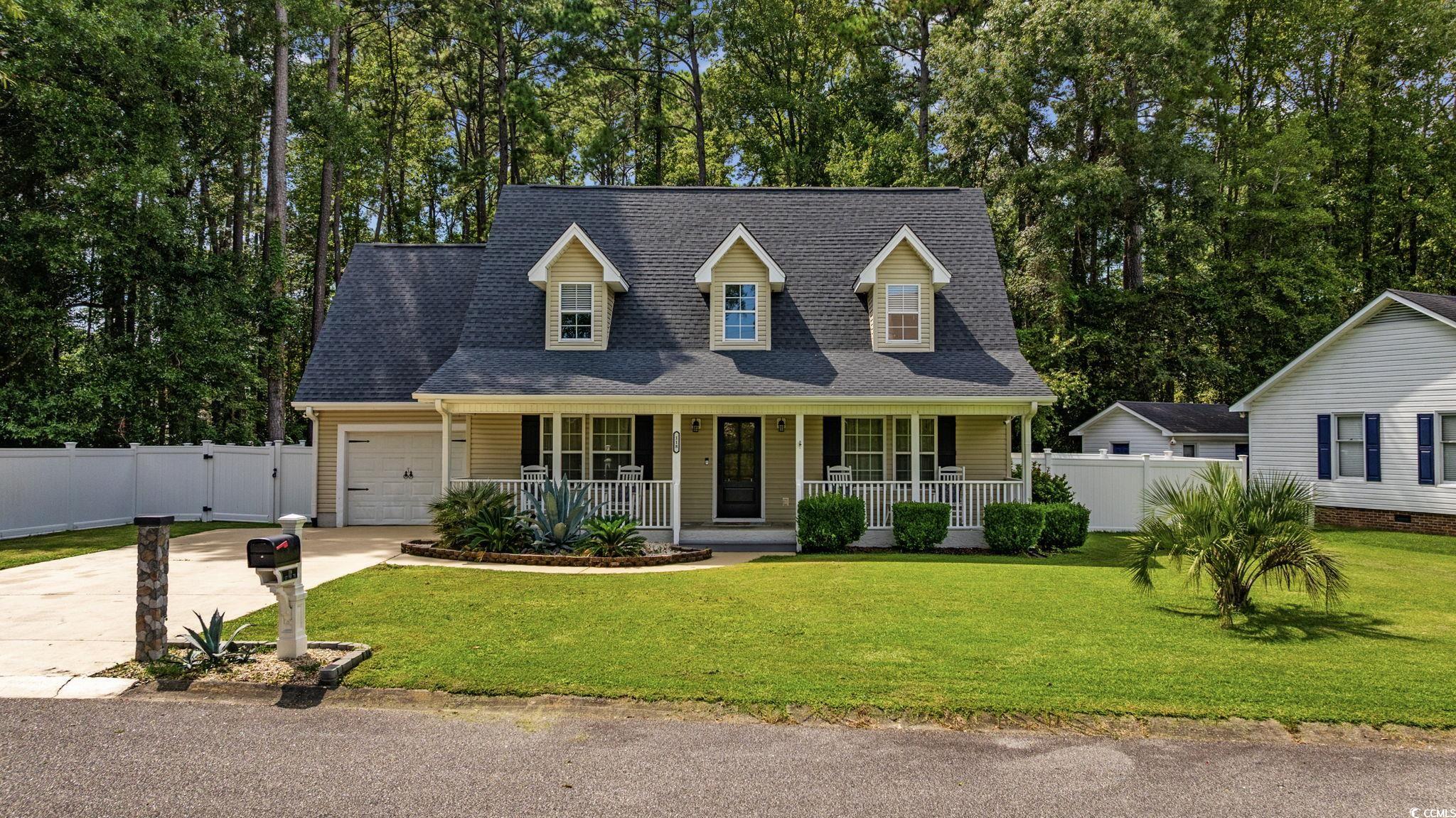 Cape cod home with roof with shingles, covered porch, driveway, and view of scattered trees