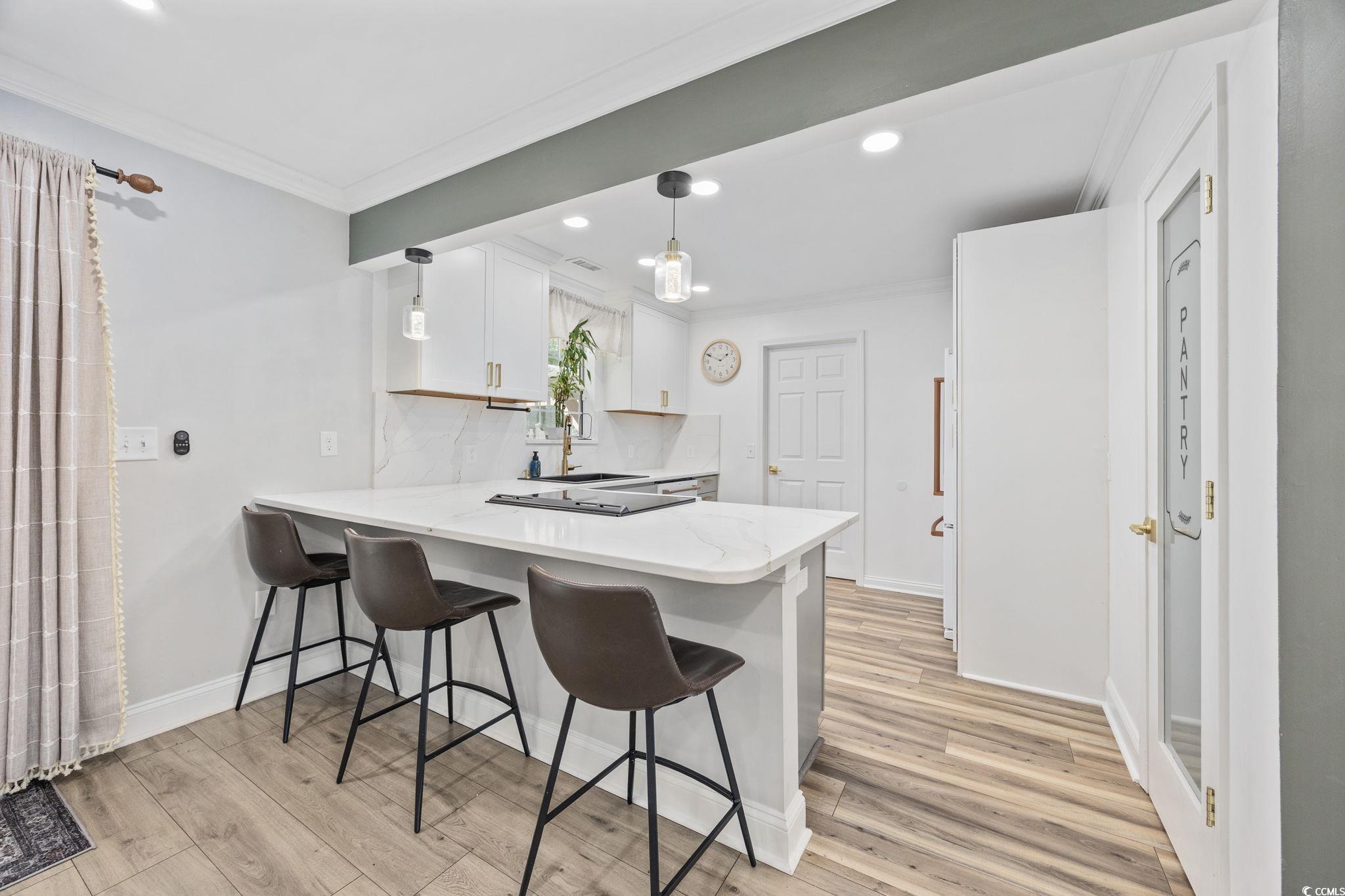 118 Sly Fox Trail Myrtle Beach, SC 29588 - Photo 13 of 40 Kitchen with a peninsula, a kitchen bar, crown molding, light wood-style floors, and decorative light fixtures