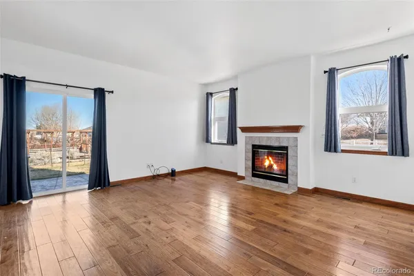 a view of an empty room with wooden floor fireplace and a window