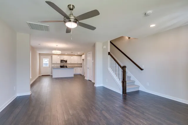 a view of an empty room with wooden floor and a ceiling fan