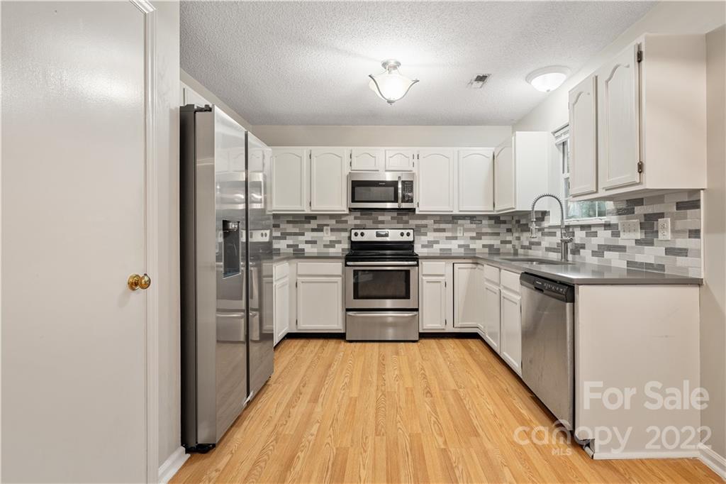 12021 Danby Road Pineville, NC 28134 - Photo 4 of 27 a kitchen with stainless steel appliances a stove top oven a sink a refrigerator white cabinets and a wooden floor