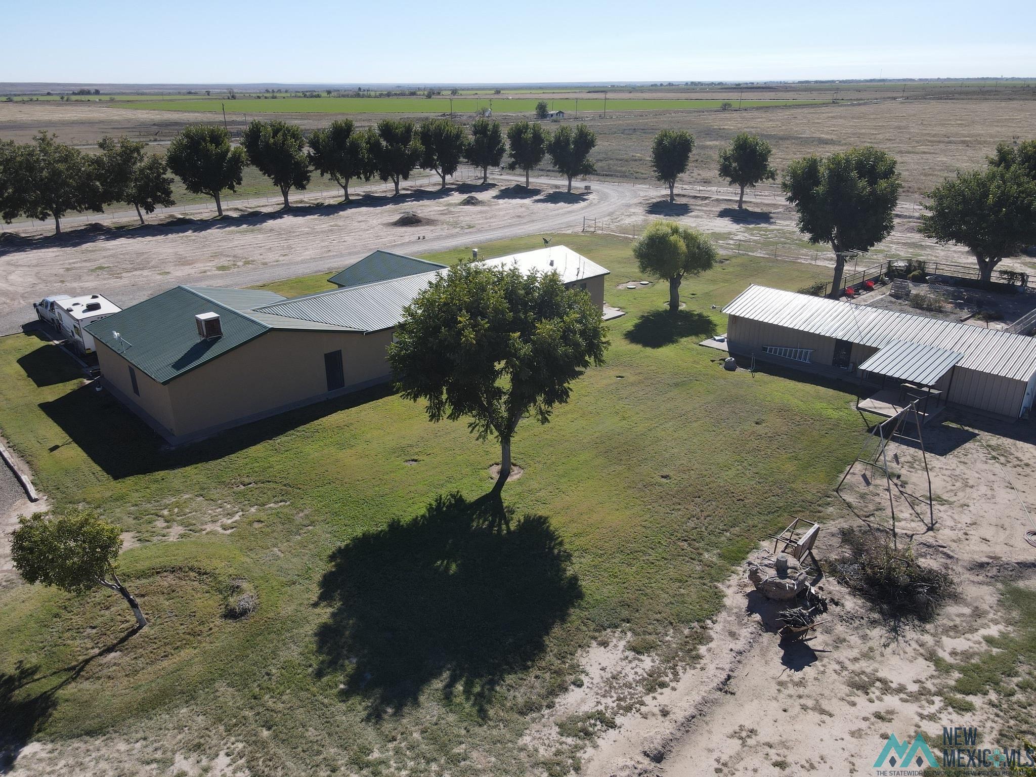 6660 Cherokee Road Dexter, NM 88230 - Photo 39 of 46 Rural property featuring a main building with a green metal roof, a secondary building with a metal roof, a gravel driveway, and scattered mature trees