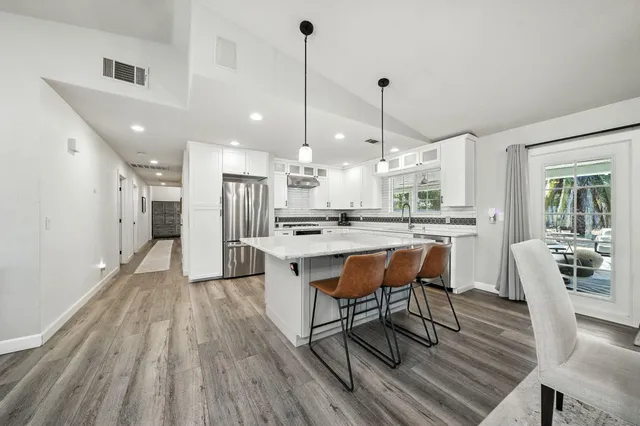 a kitchen with stainless steel appliances kitchen island granite countertop a table chairs in it and wooden floors