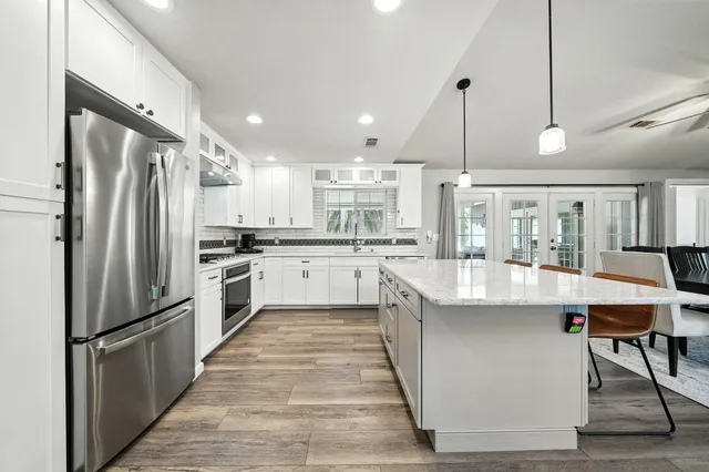 a large kitchen with stainless steel appliances kitchen island granite countertop a refrigerator a stove a sink dishwasher and white cabinets with wooden floor