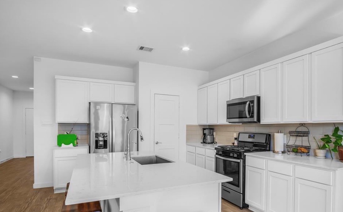 14258 Wonder Lake Lane Conroe, TX 77384 - Photo 5 of 12 a kitchen with stainless steel appliances a stove a refrigerator a sink a microwave a dining table and chairs with wooden floor