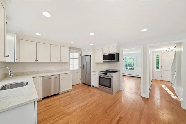 a large kitchen with stainless steel appliances granite countertop a sink dishwasher a stove and a refrigerator with wooden floor