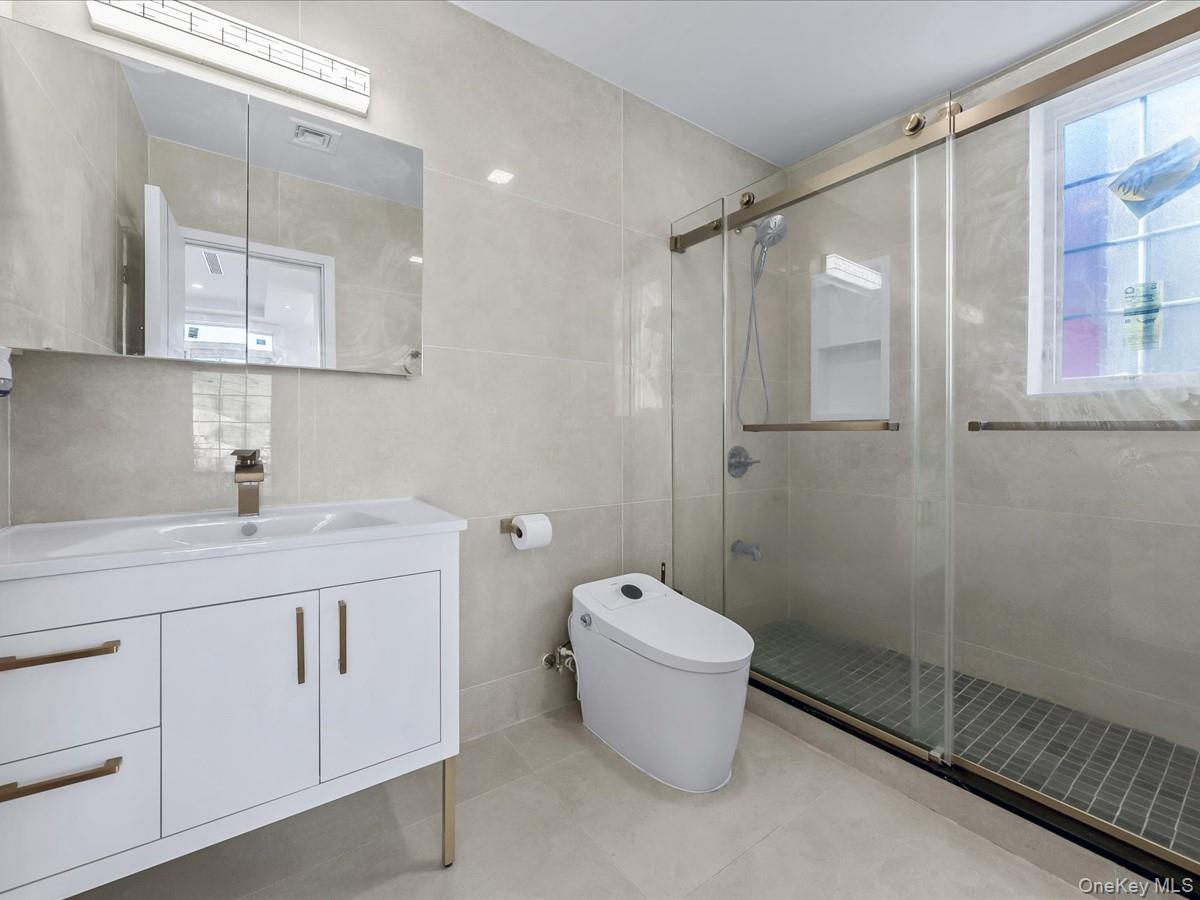 233-12 Bay Street Queens, NY 11363 - Photo 26 of 46 Full bath with tile walls, vanity, a stall shower, and light tile patterned floors